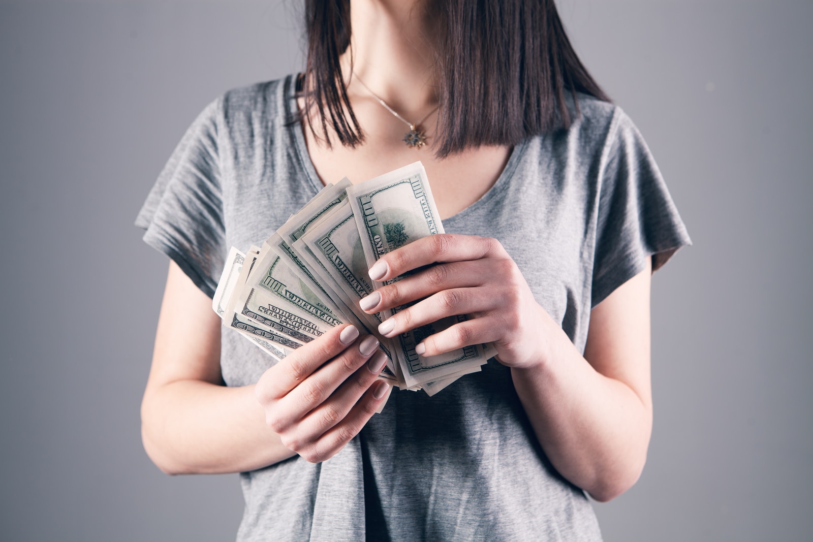 woman in gray shirt holding fan of us dollar bills