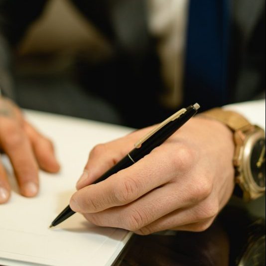 Close-Up Photo of a Person's Hand Signing a Paper